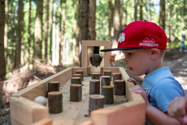 Kleiner Bub mit roter Kappe spielt mit der Waldkugelbahn. (Foto: Niki Pommer)
